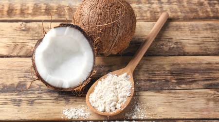Coconut and coconut flour on a wooden spoon with a whole coconut in the background.